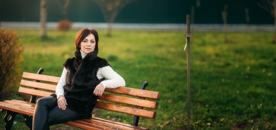Inhaltsbild: Eine Frau sitzt auf einer Bank im Park, ein Bein überschlagen, einen Arm auf der Banklehne abgestützt.