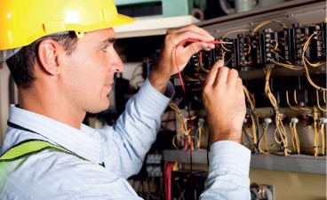 Ein Mann mit gelbem Schutzhelm prüft einen elektronischen Schaltkasten.
