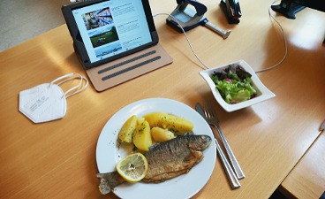 News- Bild: Fischgericht sowie Laptop und FFP2- Maske auf einem Schreibtisch