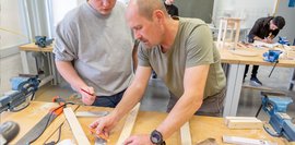 Galeriebild: Kursteilnehmer bekommt in Holzwerkstatt Unterstützung bei der Markierung eines Brettes.