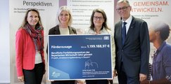 Das Bild zeigt vier Personen, die in einem Raum stehen und einen Förderbescheid über 1.199.188,97 € präsentier Im Hintergrund sind Plakate mit den Worten „Wir eröffnen Perspektiven“ und „Zukunft. Gemeinsam. Entwickeln.“ zu sehen.