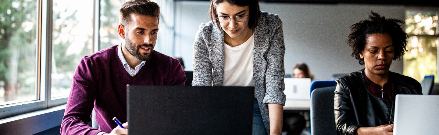 AoG-plus-TQ: Innovative Wege zur Qualifizierung und Fachkräftesicherung Header: Personen arbeiten gemeinsam in einem modernen Büro an Laptops. Eine Frau steht und unterstützt sie bei der Arbeit.