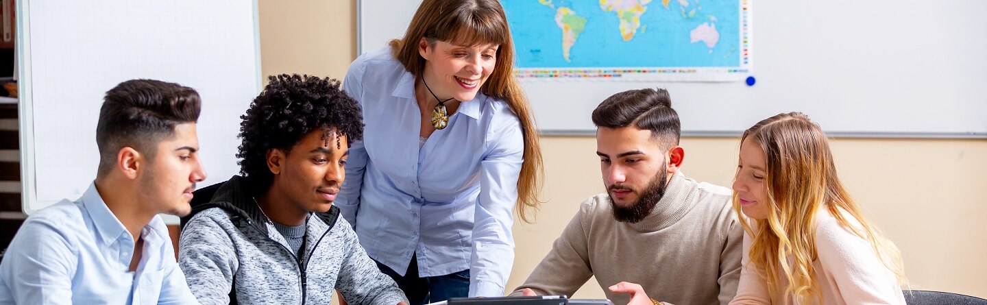 Berufswahl Lokal Header: Schülergruppe sitzt an einem Tisch und arbeitet mit Tablets, während eine Lehrkraft daneben steht und unterstützt.
