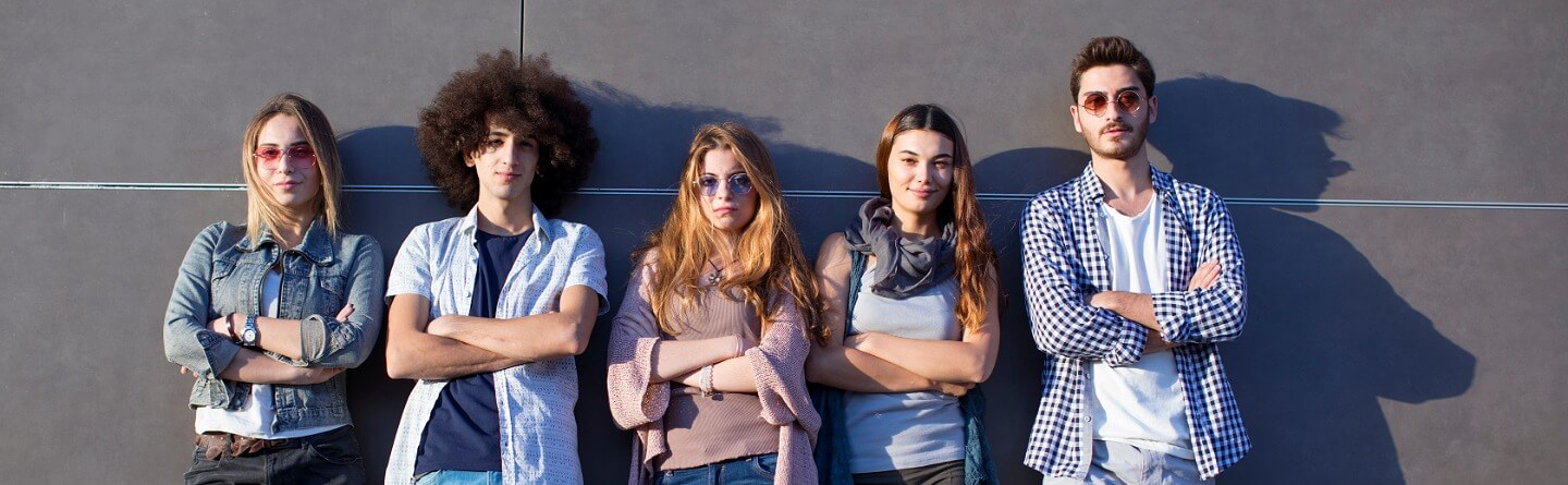 Jugendliche stehen lässig vor einer modernen grauen Wand, Arme verschränkt, in Freizeitkleidung wie Jeans und Hemden.