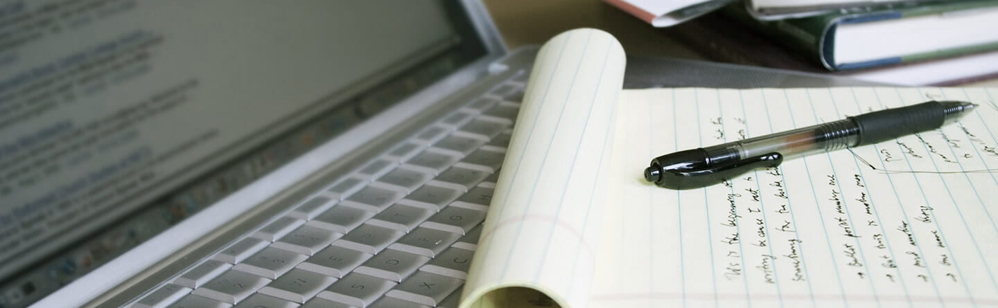 Header: Laptop mit Notizblock, Stift und Büchern, das oberste aufgeschlagenen