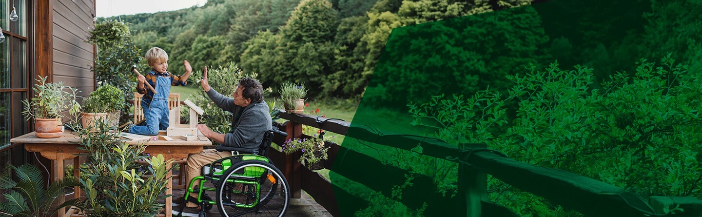 Berufsanerkennung Ergotherapie Header: Ein Mann im Rollstuhl und ein Kind geben sich auf einer Terrasse ein High Five.