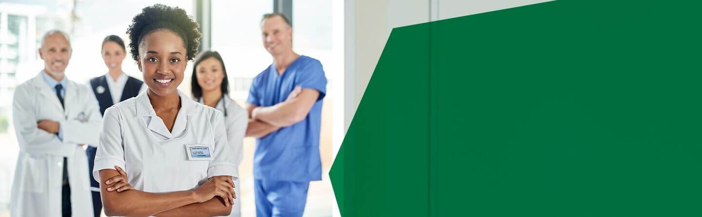 Berufsanerkennung Pflege Header: Eine Pflegefachfrau lächelt in die Kamera, im Hintergrund weiteres Pflegepersonal.