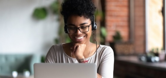 Afroamerikanische Frau sitzt am Laptop und lernt Deutsch via Online-Unterricht