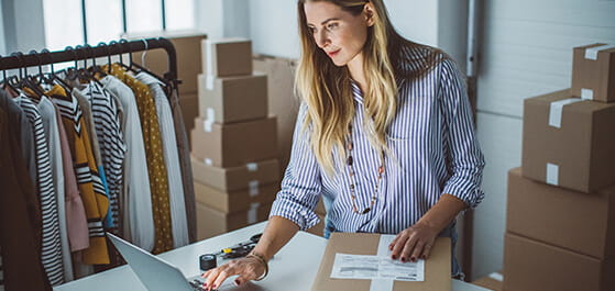 Inhaltsbild: Besitzerin eines kleinen Geschäfts packt Kleidung in Kartons, die sie für den Versand vorbereitet. 
