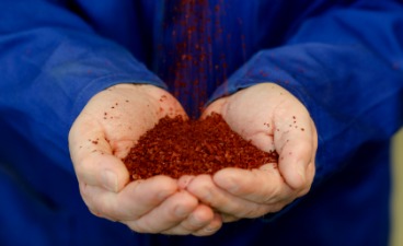 Zwei Hände halten eine Handvoll roter Kunststoffteile, die langsam von oben in die Finger rieseln.
