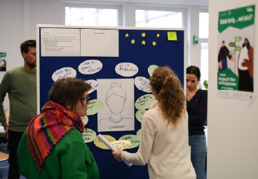 Workshop: Zwei Personen stehen vor einer Pinnwand und hängen Zettel auf.