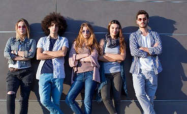 Jugendliche stehen lässig vor einer modernen grauen Wand, Arme verschränkt, in Freizeitkleidung wie Jeans und Hemden.