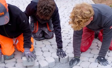 Drei Jugendliche setzen gemeinsam Pflastersteine und arbeiten konzentriert an einer praktischen Aufgabe im Freien.