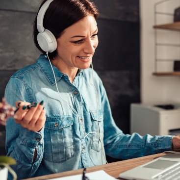Lächelnde Frau mit Headset an Schreibtisch spricht in den Bildschirm.