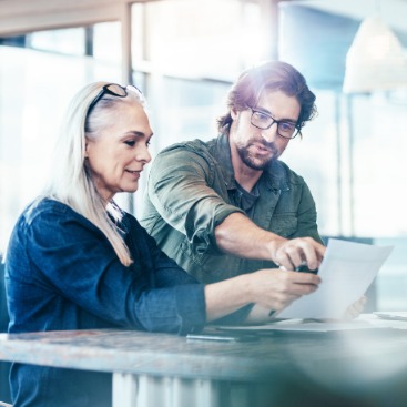 Ein Mann zeigt einer Frau etwas auf einem Papier in moderner Büroumgebung.