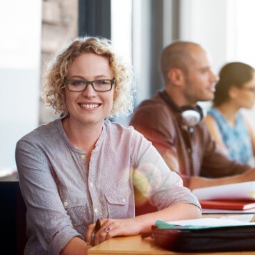 Schulungsraum mit mehreren Personen, Frau blickt in die Kamera.