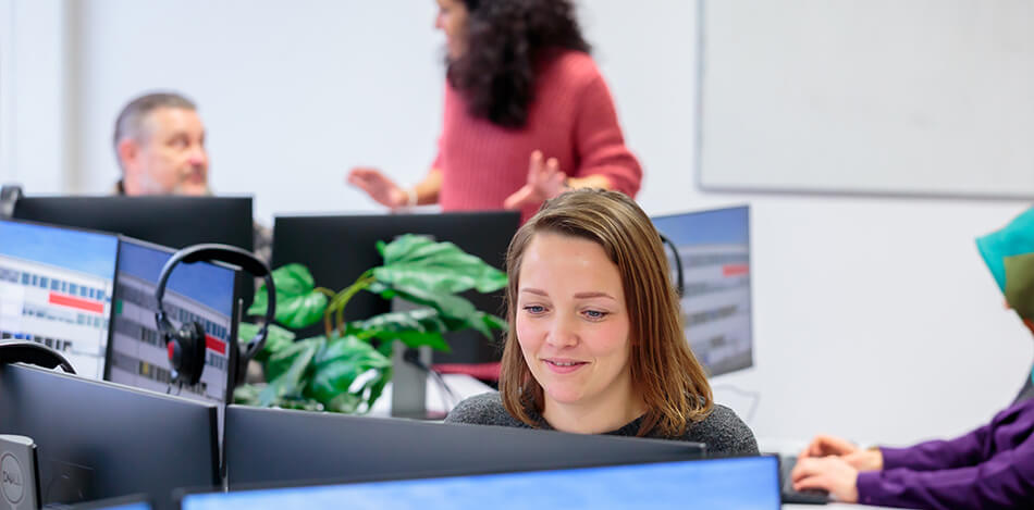 Galeriebild: Mehrere Personen sitzen vor Computer mit Doppelmonitoren.