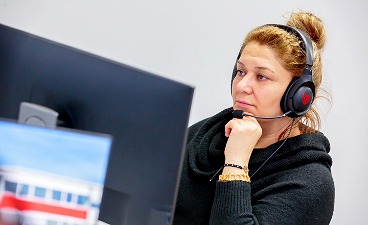 Frau sitzt mit Kopfhörer und Mikrofon vor einem Computer