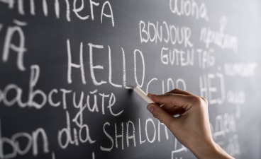 Eine Person schreibt auf eine Tafel "Hallo" in verschiedenen Sprachen 