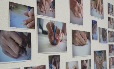 Auf dem Bild ist eine Fotoausstellung mit mehreren kleinen Fotos zu sehen. Die Fotos zeigen immer eine Hand, die einen Stift in der Hand hält und schreibt.