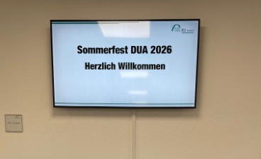 Das Bild zeigt einen Bildschirm, auf welchem der Text: "Sommerfest DUA 2026 Herzlich Willkommen" eingeblendet ist.