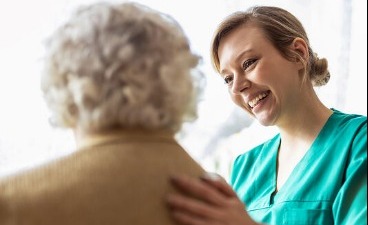 Pflegekraft legt die Hand auf den Rücken einer Seniorin