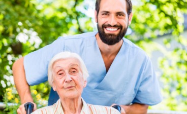 Eine Betreuungskraft schiebt eine Seniorin im Rollstuhl.