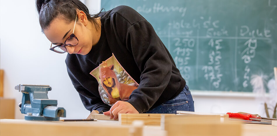 Inhaltsbild: Eine junge Frau bearbeitet ein Stück Holz.