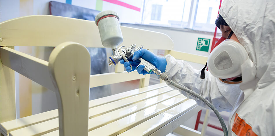 Inhaltsbild: Ein junger Teilnehmer lackiert mit der Spritzpistole eine Bank.