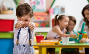 Im Hintergrund spielen mehrere Kinder, vorne steht ein Junge und zeigt den Daumen nach oben