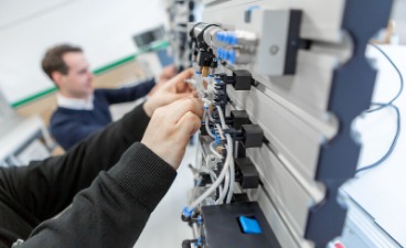 Eine Person arbeitet an einer Elektro-Schalteinheit. Eine zweite Person macht das gleiche im Hinteregrund.