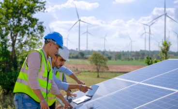 Zwei Männer stehen vor einer Solaranlage und deuten auf ein Laptop.