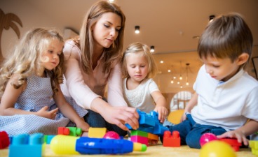 Junge Frau sitzt am Boden und spielt mit drei Kindern