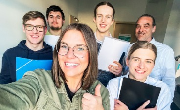 Gruppe junger Menschen schauen glücklich und zuversichtlich und haben Unterlagen in den Händen.