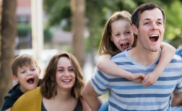 Eine junge Familie hat ihre beiden Kinder auf den Schultern und sie sehen gemeinsam in Richtung Zukunft während sie nebeneinander laufen.