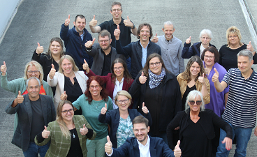 News- Foto: Ein Gruppenfoto vieler lächelnder Menschen, die alle den Daumen nach oben zeigen