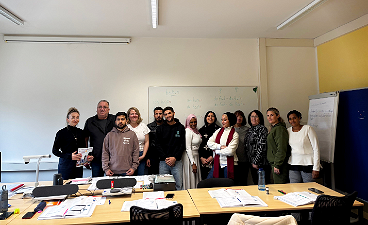 News- Foto: Eine Gruppe bestehend aus Männern und Frauen posiert in einem Klassenzimmer vor der Wand stehend