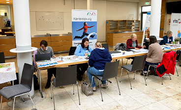 News- Foto: Mehrere Personen sitzen an einer Tischreihe, hinter ihnen ein Rollup