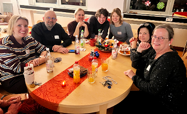 News- Foto: Mehrere Personen sitzen um einen festlich geschmückten Tisch zusammen und posieren für das Foto