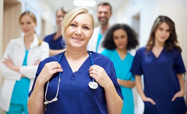 Frau mit blauem Kittel und Stethoskop um den Hals und weiteren ähnlichen Personen im Hintergrund