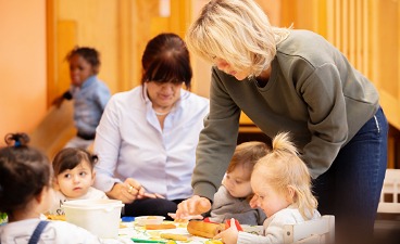 Zwei Frauen kümmern sich um Kleinkinder, die am Tisch sitzen
