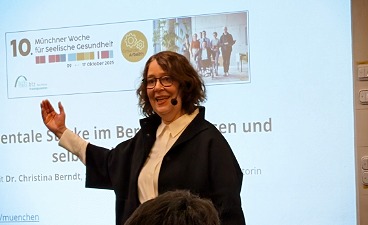 Frau hält stehend einen Vortrag vor einer Leinwand mit Präsentation