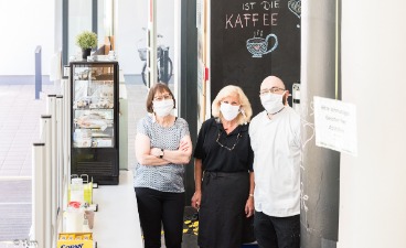 News-Bild: 3 Menschen mit Mund-Nase-Schutz stehen an der Essensausgabe des Cafe Gusto.