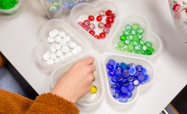 Einsetzkasten mit Perlen unterschiedlicher Farben in einem Herzform-Behältnis.