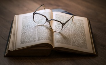 Auf einem aufgeschlagenem Buch liegt eine Brille. 
