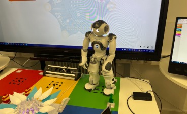 Ein Roboter steht auf einem Schreibtisch, im Hintergrund ein Monitor