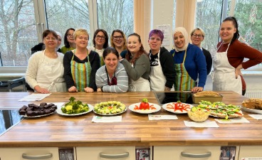 Eine Gruppe von Frauen mit Kochschürzen stehen hinter einem Buffet. 