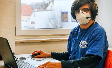 Teaserbild: Jugendlicher sitzt mit Headset und Maske am Laptop.