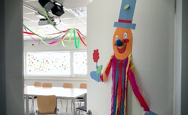 News- Bild: Eine mit einem Clown beklebte Tür, welche in ein geschmücktes Klassenzimmer führt