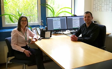 News- Bild: Zwei bfz- Mitarbeiter posieren sich am Schreibtisch gegenübersitzend
